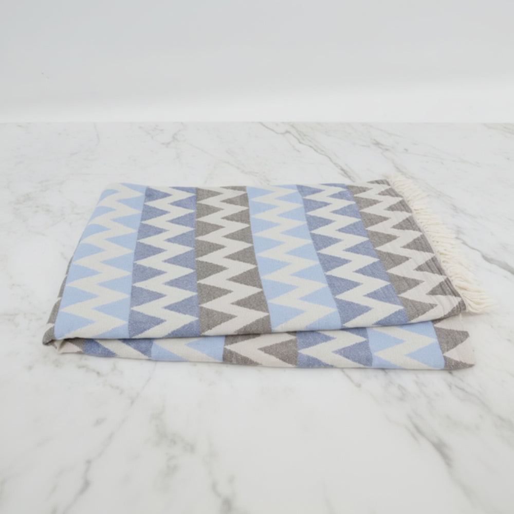 A folded organic turkish towel beach towel in light blue gray and white zigzag pattern with fringed edges 36x78