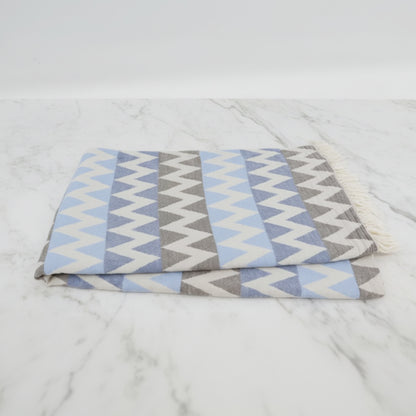 A folded organic turkish towel beach towel in light blue gray and white zigzag pattern with fringed edges 36x78