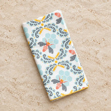 Folded white cotton bee cloth napkin with vibrant orange black bees light blue hexagons and gray paisley design