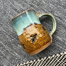 This handmade pottery mug features a warm mustard honeycomb base with an adorable bee design and sea foam blue rim. 
