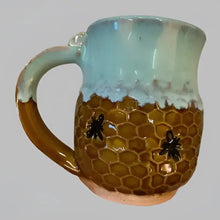 This handmade pottery mug features a warm mustard honeycomb base with an adorable bee design and sea foam blue rim. 