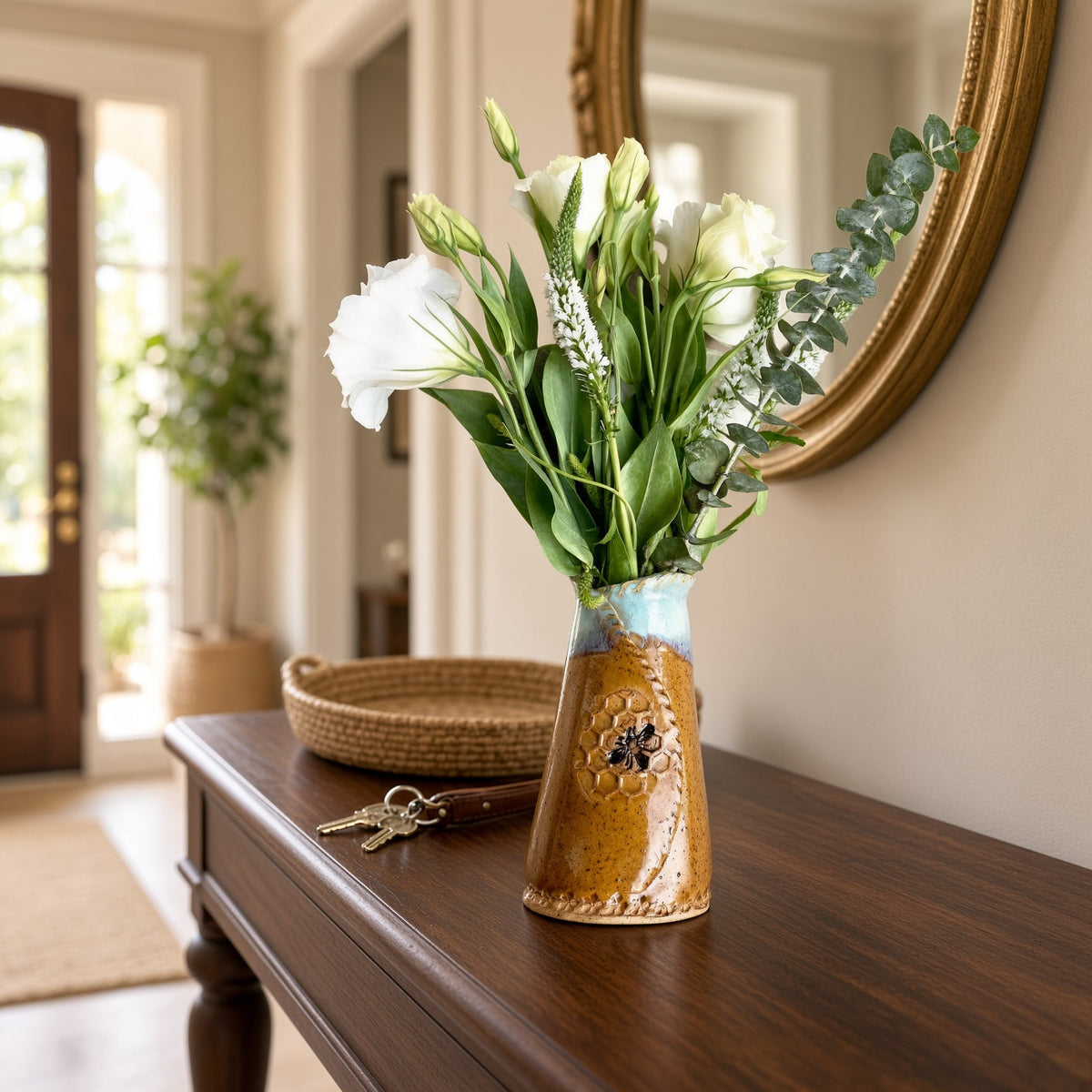 A 6 inch tall bee vase with a rustic ceramic mustard honeycomb pattern and blue rim holding white flowers