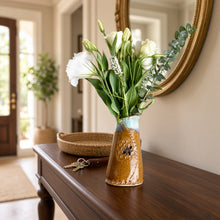 A 6 inch tall bee vase with a rustic ceramic mustard honeycomb pattern and blue rim holding white flowers
