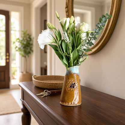 A 6 inch tall bee vase with a rustic ceramic mustard honeycomb pattern and blue rim holding white flowers