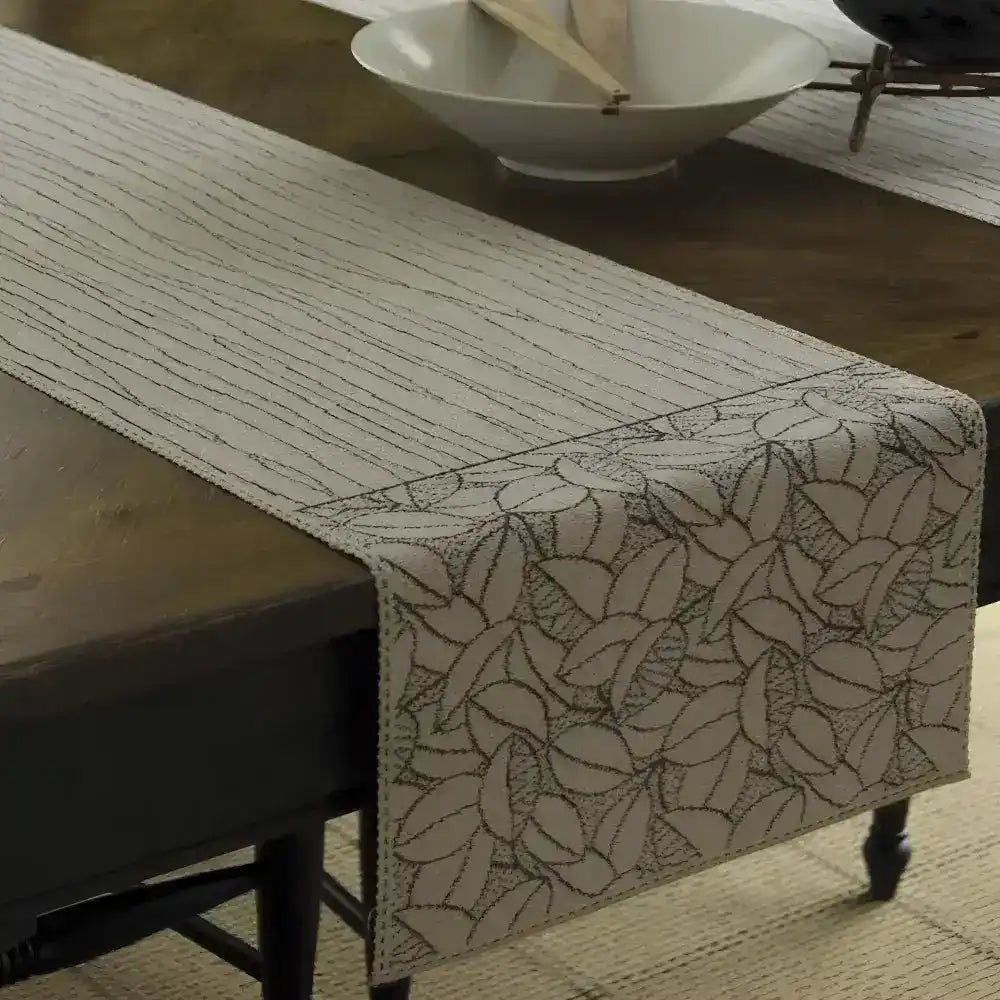 Beige table runner with black woven design of lines and leaves.