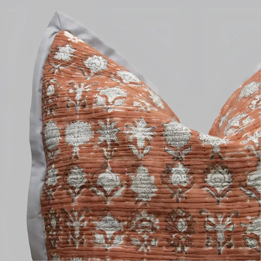 Pillow cover features a rusty-peach colored cotton gauze material with a hand block print design in a neutral color and has a zipper closure on the back side.
