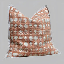 Pillow cover features a rusty-peach colored cotton gauze material with a hand block print design in a neutral color and has a zipper closure on the back side.