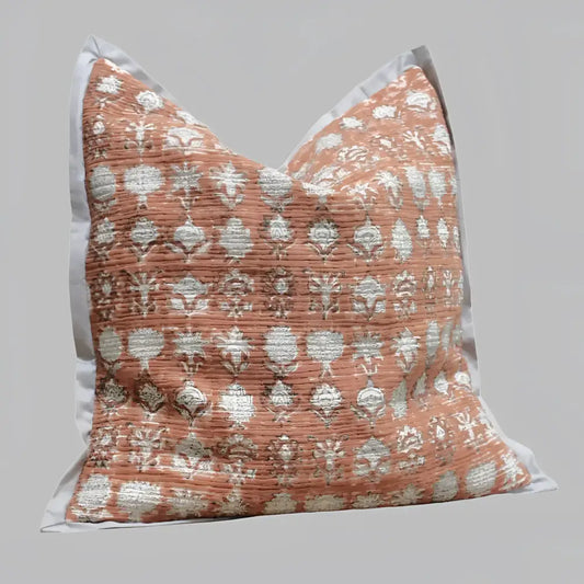 Pillow cover features a rusty-peach colored cotton gauze material with a hand block print design in a neutral color and has a zipper closure on the back side.