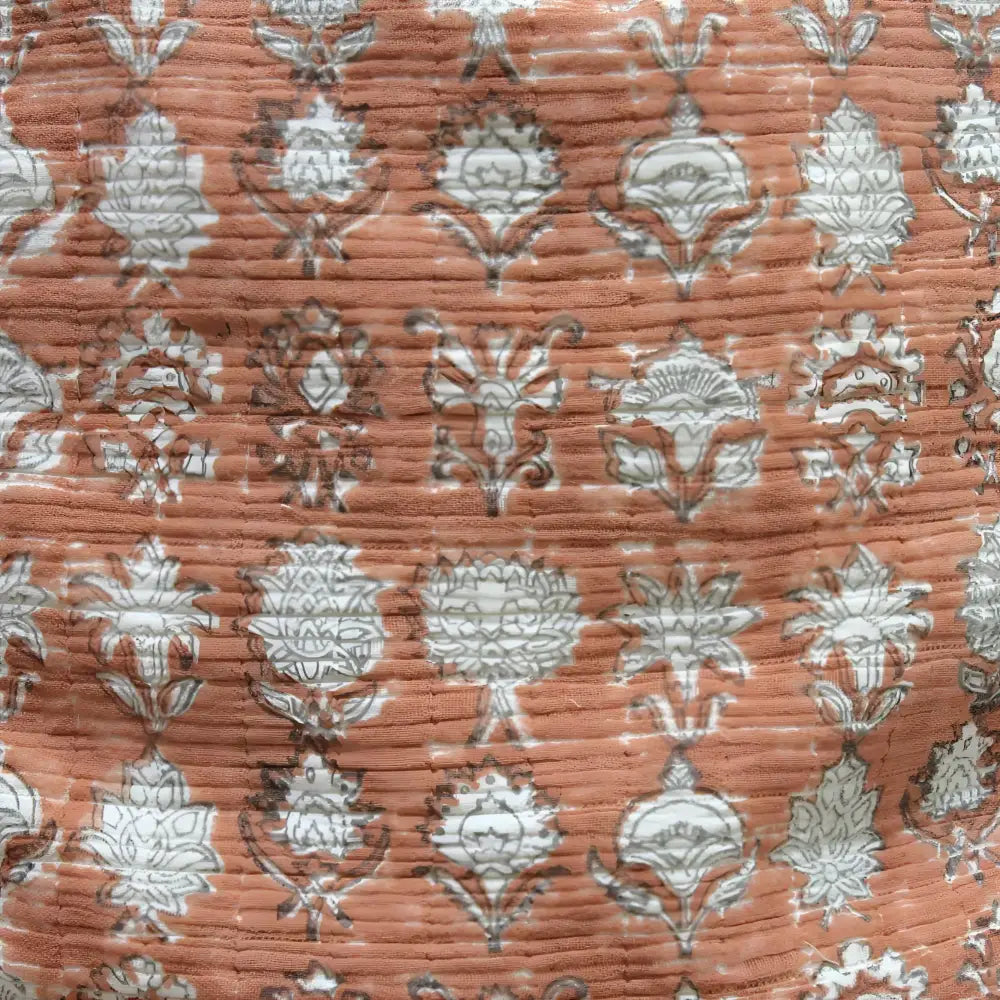 Pillow cover features a rusty-peach colored cotton gauze material with a hand block print design in a neutral color and has a zipper closure on the back side.