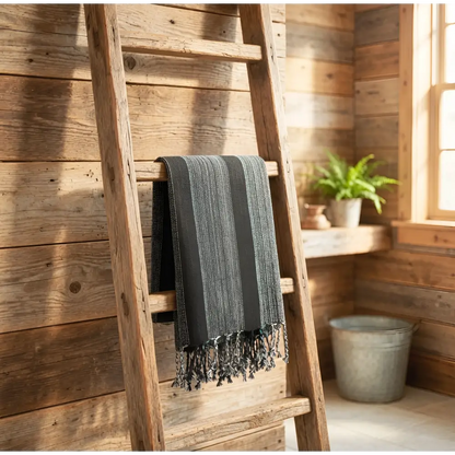 A dark gray bold stripes towel turkish towel handwoven striped towel hanging on a rustic wooden ladder with fringed edges