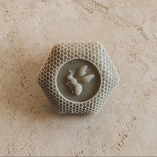 A hexagonal light gray handmade soap with honeycomb texture and raised bee featuring french green clay and artisan wild honey