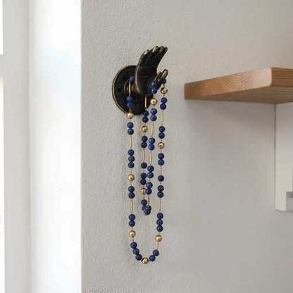 A navy blue and gold beaded rosary hanging from a brass mini mudra hand jewelry holder with bronze hand hooks
