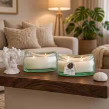 Two translucent green bubble glass candle holders with white driftwood sea salt candles lit with three wicks each
