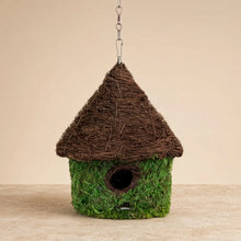 A charming woven sanctuary bungalow birdhouse with green moss body and brown thatched roof to invite backyard birds