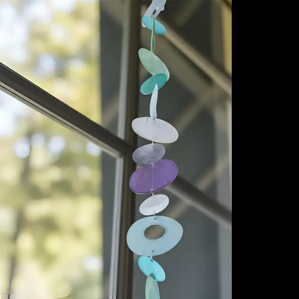 A colorful capiz strand wind chime in blue purple and green with translucent discs to watch light dance beautifully