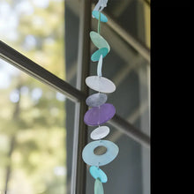 A colorful capiz strand wind chime in blue purple and green with translucent discs to watch light dance beautifully