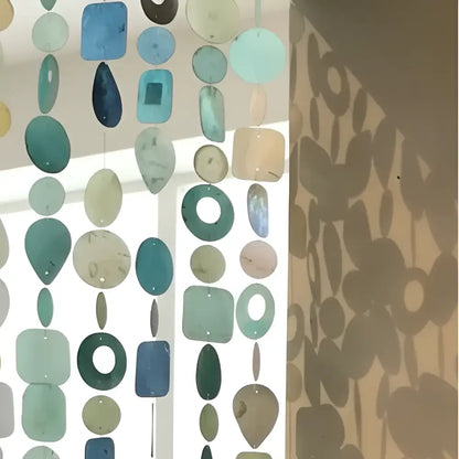 A handmade eco-friendly capiz strand curtain with translucent hand-cut glass pieces in teal blue and green shades
