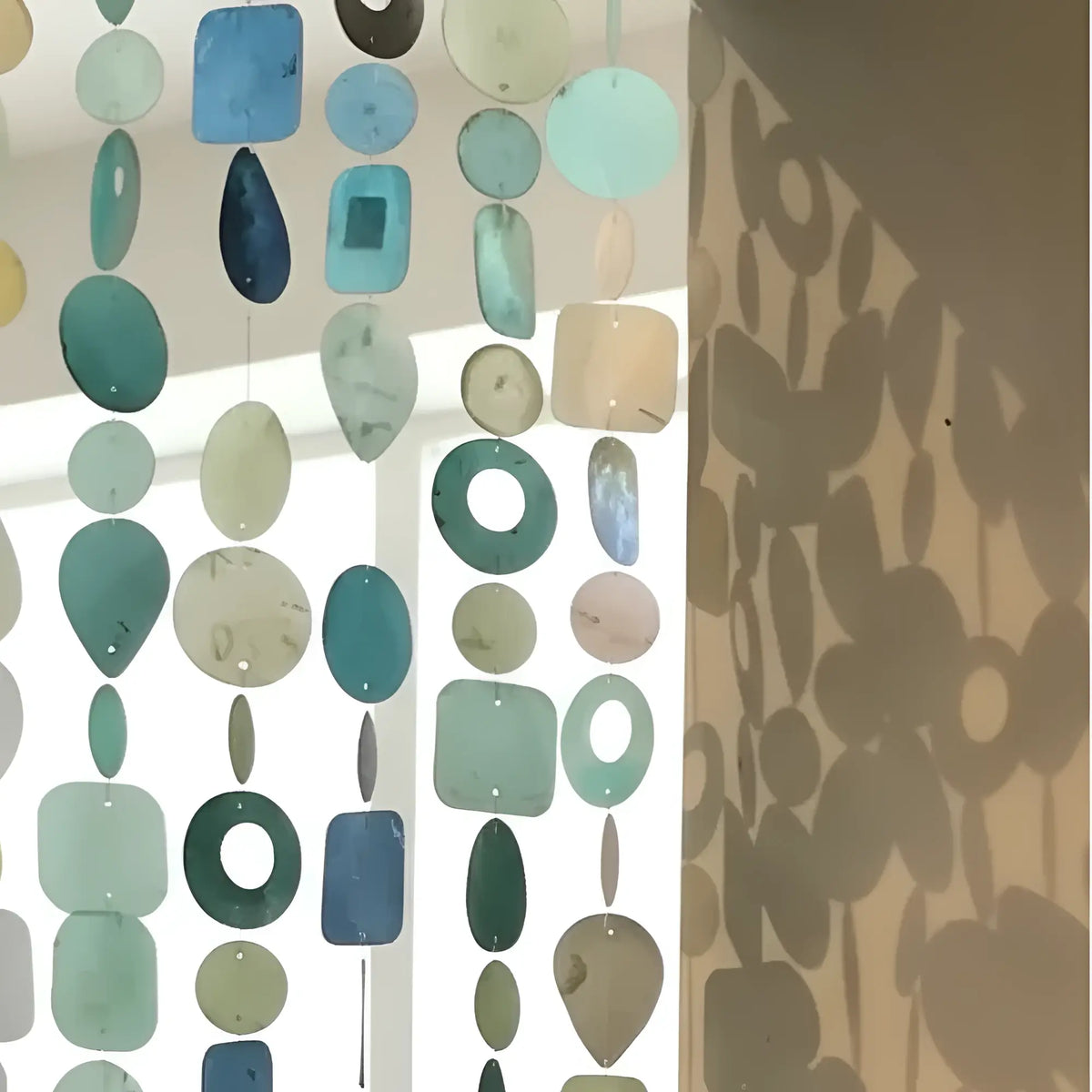 A handmade eco-friendly capiz strand curtain with translucent hand-cut glass pieces in teal blue and green shades