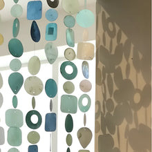 A handmade eco-friendly capiz strand curtain with translucent hand-cut glass pieces in teal blue and green shades