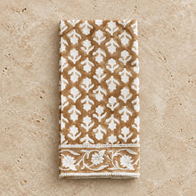 A folded caramel block print cotton napkin with brown and white floral patterned border in a set of 4