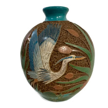 Carved ceramic vase with heron bird designs on a white background.