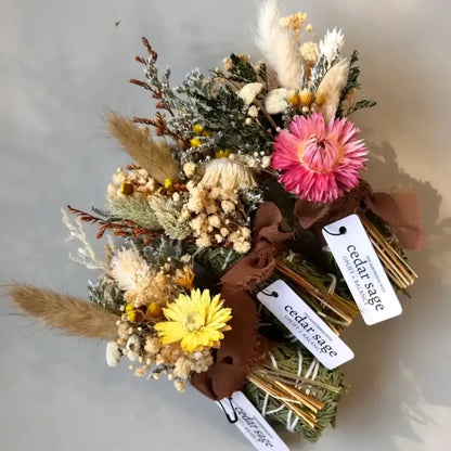 A vibrant cedar sage bundle smudge stick with pink flower yellow daisy and natural textures for grounding energy smoke cleansing
