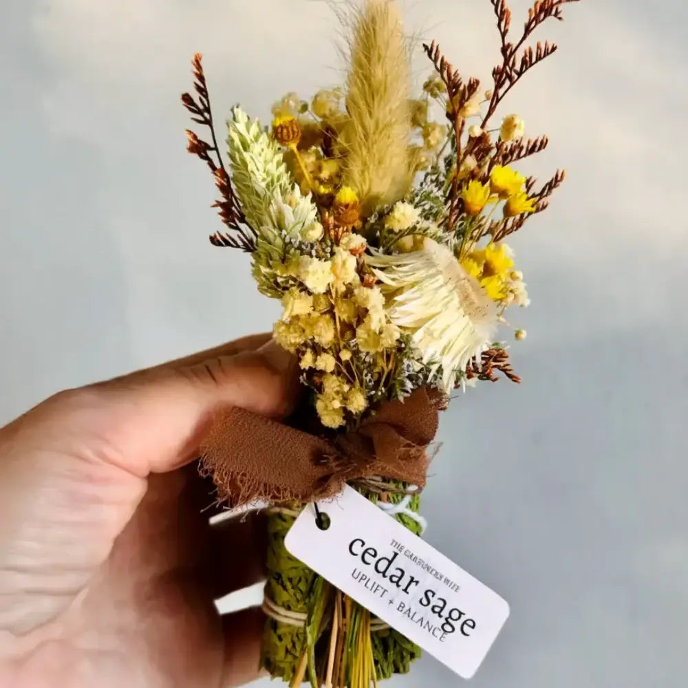 A cedar sage bundle smudge stick with soft yellow flowers pampas grass and brown leather ribbon for grounding energy and smoke cleansing
