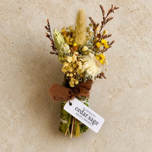 A rustic cedar sage bundle smudge stick with yellow blossoms brown stems and pampas grass for smoke cleansing and grounding energy