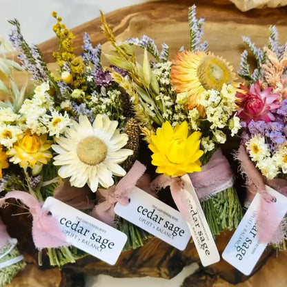A vibrant cedar sage bundle smudge stick with dried yellow white purple and pink flowers wrapped in lavender ribbon for smoke cleansing and grounding energy