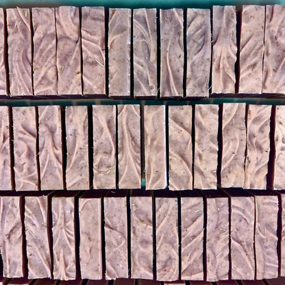 Rows of handmade cedar wood exfoliating bar soap in soft purple with leaf patterns and natural red clay texture