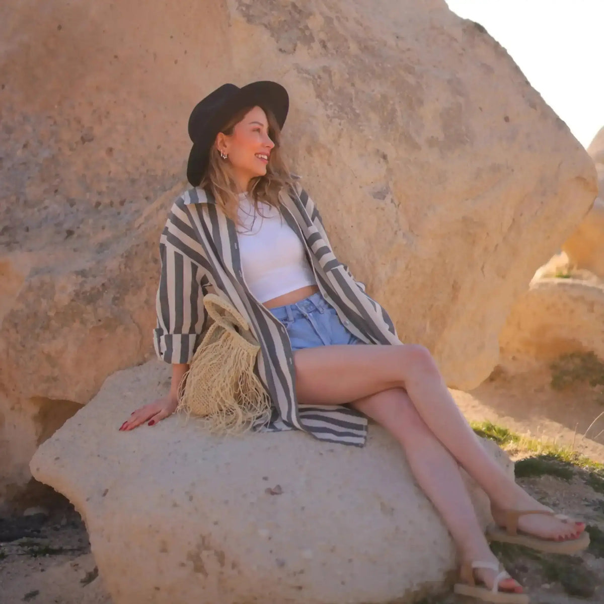 Woman in striped linen cotton blend shirt dress cover sitting on a rock relaxing outdoors