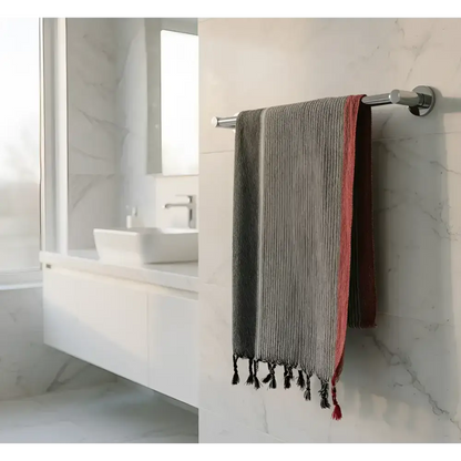 A ruby striped turkish cotton towel in charcoal white and red with black tassels hanging on a chrome rack