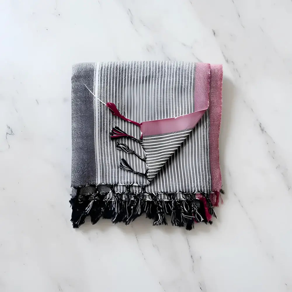 Folded charcoal white and ruby striped turkish hand towel with pink border black fringe and decorative tassels