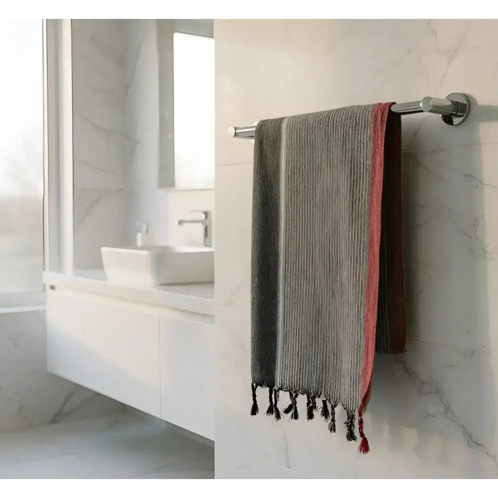 A ruby striped turkish cotton towel in charcoal white and red with black tassels hanging on a chrome rack