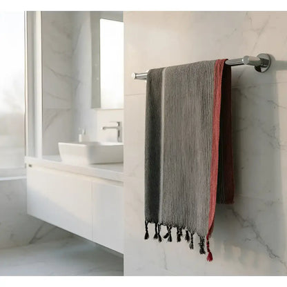 A ruby striped turkish cotton towel in charcoal white and red with black tassels hanging on a chrome rack