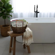 Woven brown basket filled with colorful clay milk bath soak packets featuring bentonite clay and clary sage for calmness