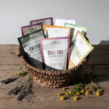 A woven brown basket filled with colorful clay milk bath packets featuring australian sandalwood and ylang ylang scents