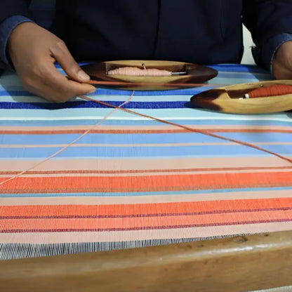 A handmade climate warming table runner with vibrant blue orange and pink stripes woven on a wooden loom