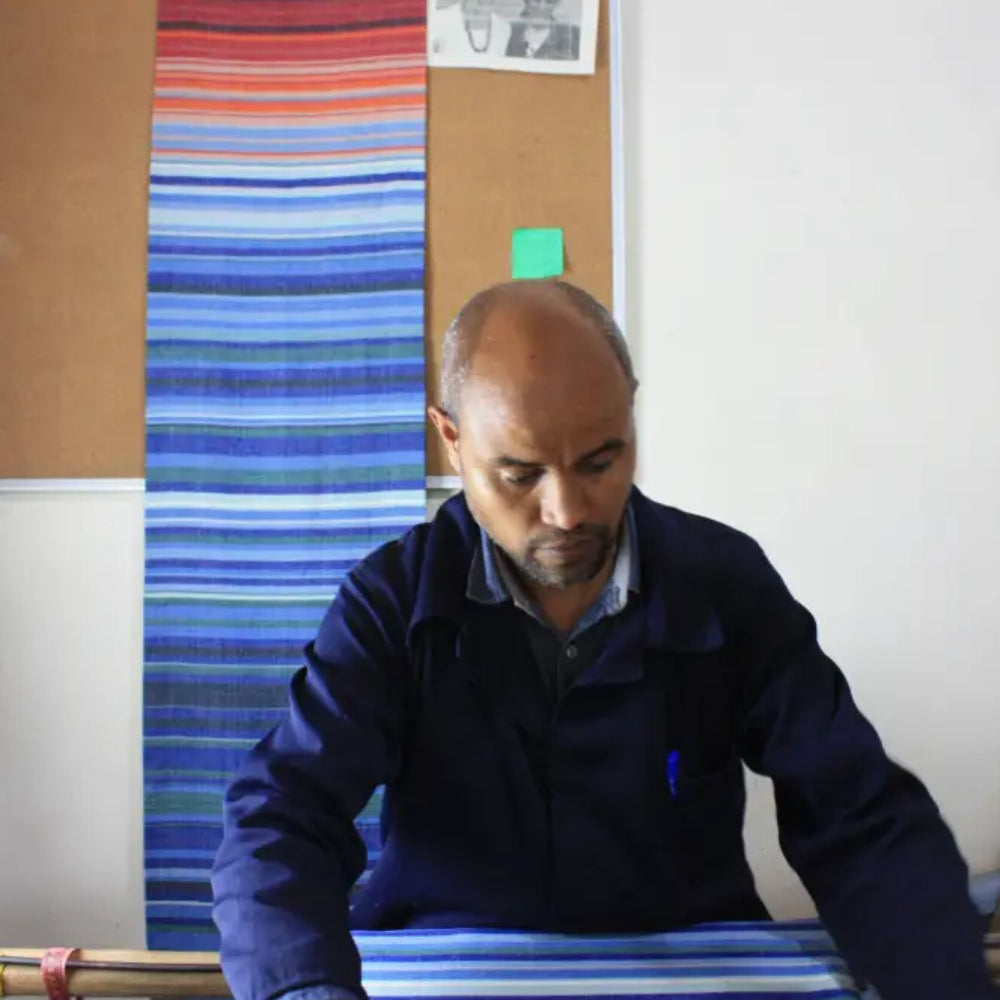 A man in a dark blue jacket weaving a handmade climate warming ethiopian handwoven table runner with bright stripes