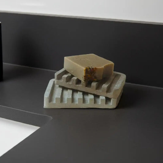 Two stacked light-colored ribbed concrete soap trays with a bar of soap on top