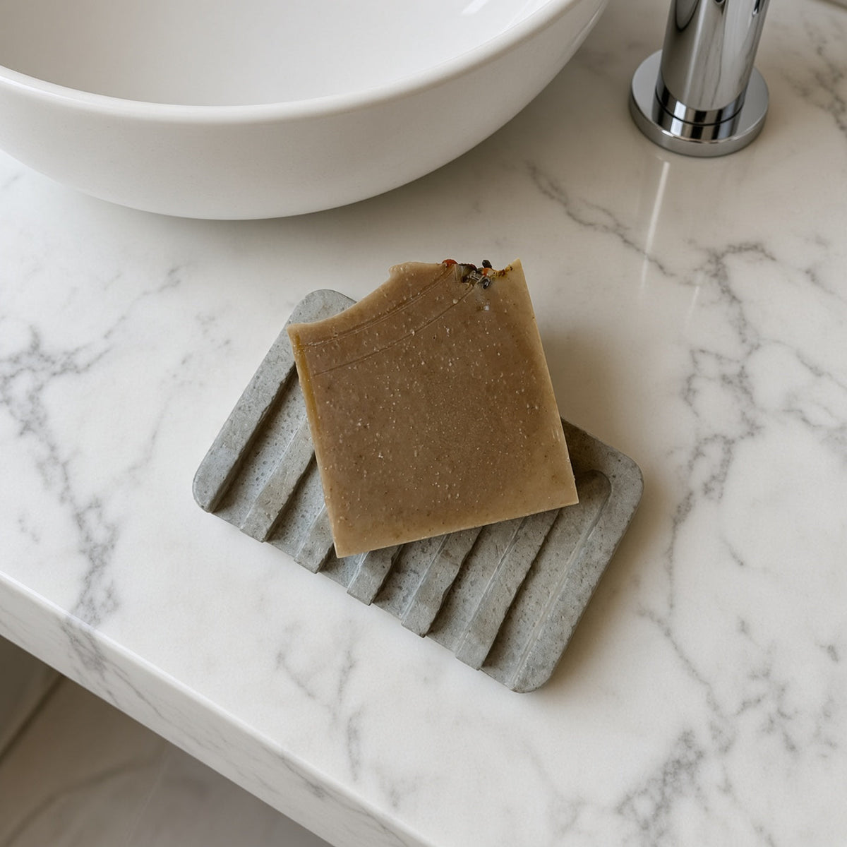 A beige speckled soap bar resting on a gray hand poured concrete soap tray for bathroom use
