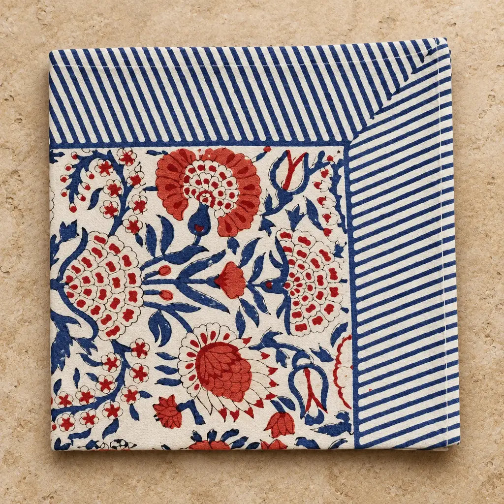 Cotton block print cotton napkins with vibrant red and blue floral pattern and navy striped border on off-white background