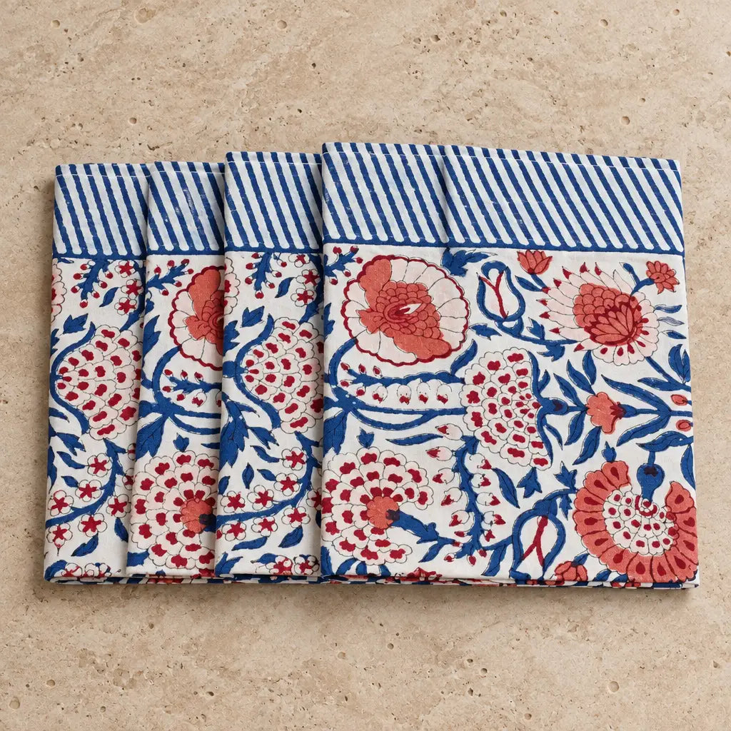 Set of four white cotton napkins with vibrant red and blue floral patterns and striped border in traditional indian block print style