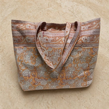 A peach-colored cotton canvas tote bag with hand block printing and rashmi orange pattern in muted floral tones
