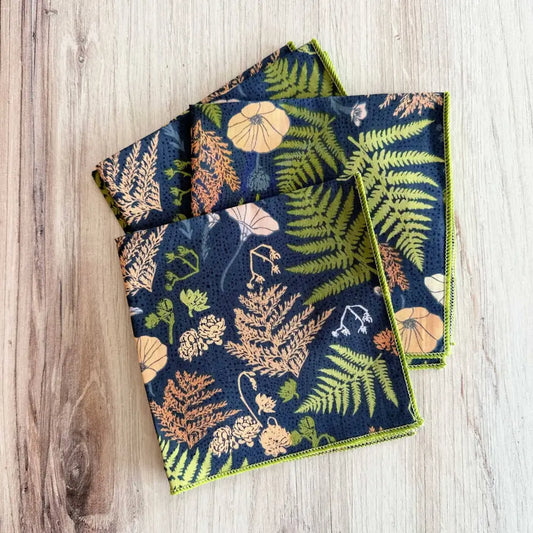 Set of three folded fabric napkins with floral and fern pattern on a wooden surface