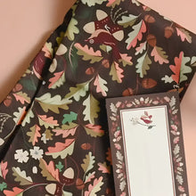Cotton tea towel with leaves features a dark brown fabric and whimsical autumn oak leaf and acorn pattern