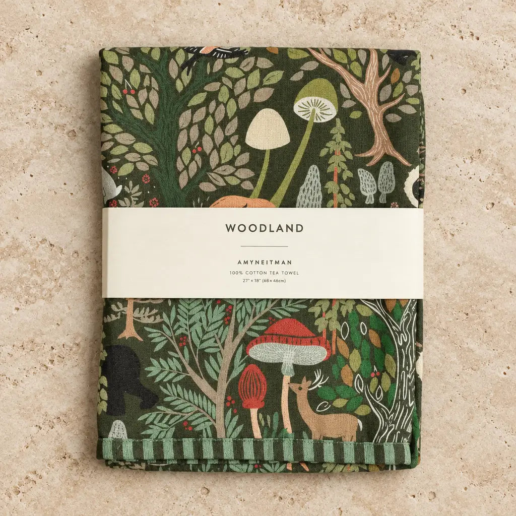 A folded dark green cotton tea towel with woodland charm featuring mushrooms deer and trees in red beige and light green