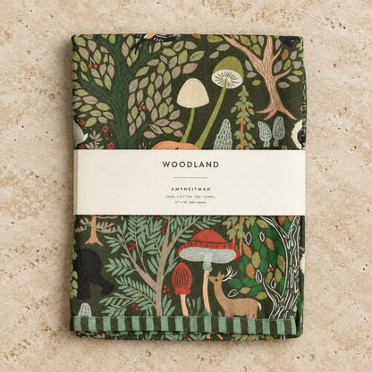 A folded dark green cotton tea towel with woodland charm featuring mushrooms deer and trees in red beige and light green