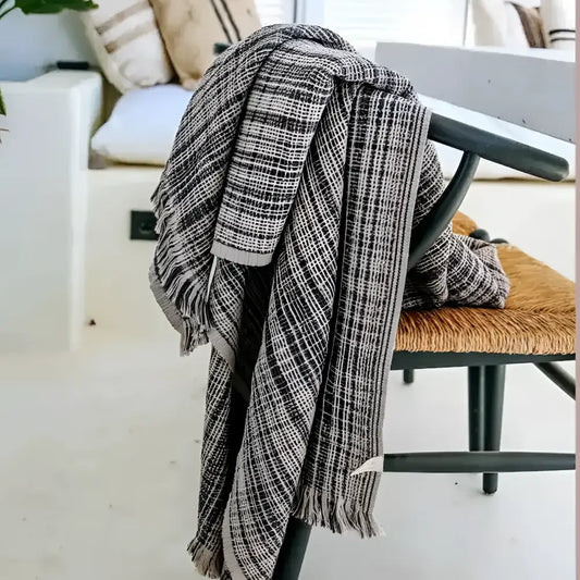Plaid blanket draped over a chair in a room with a couch and pillows.