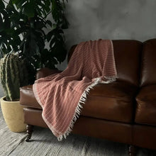 A copper colored throw blanket with off-white stripes.